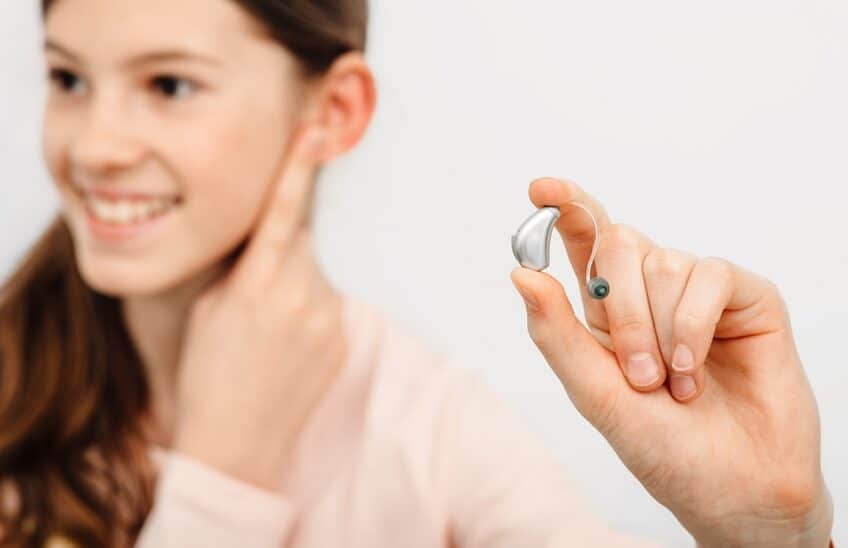 Hearing Solution For Children. Girl Holding A Hearing Aid, Treat